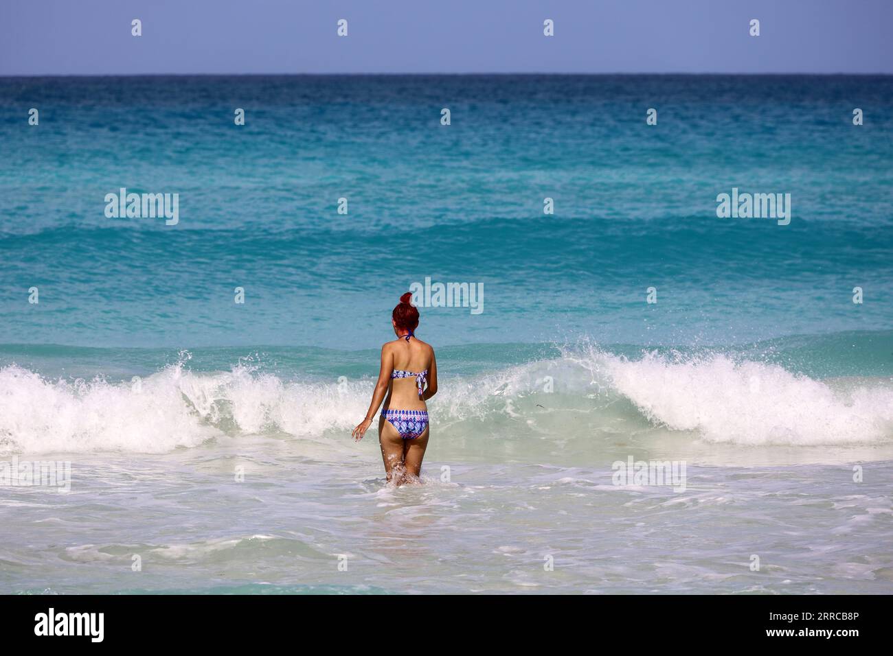 Fille en maillot de bain allant nager dans l'eau de mer azur. Vacances à la plage sur la côte ensoleillée Banque D'Images