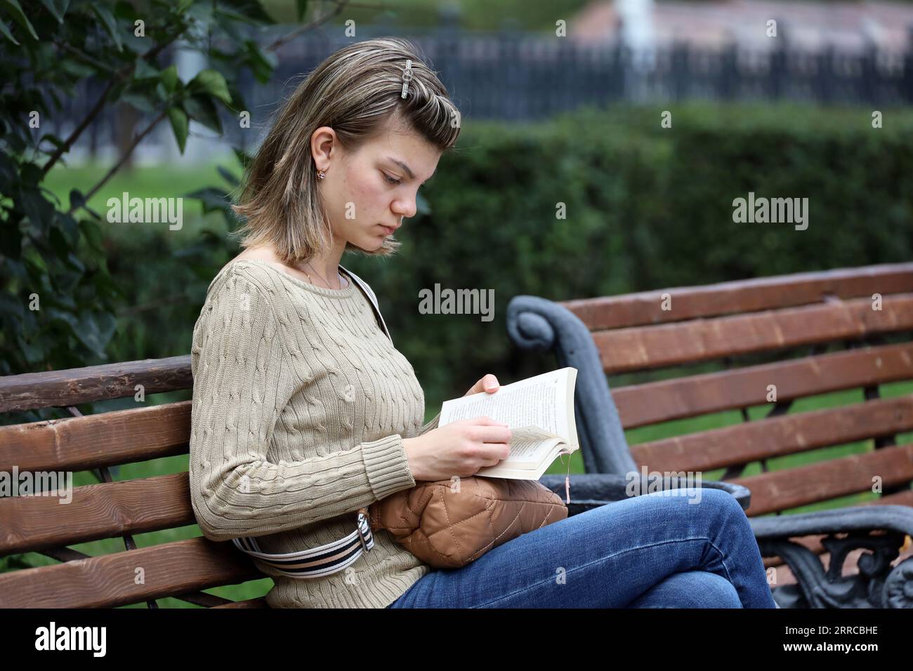 Fille assis sur un banc de rue et de lecture de fond de livre dans le parc d'automne Banque D'Images