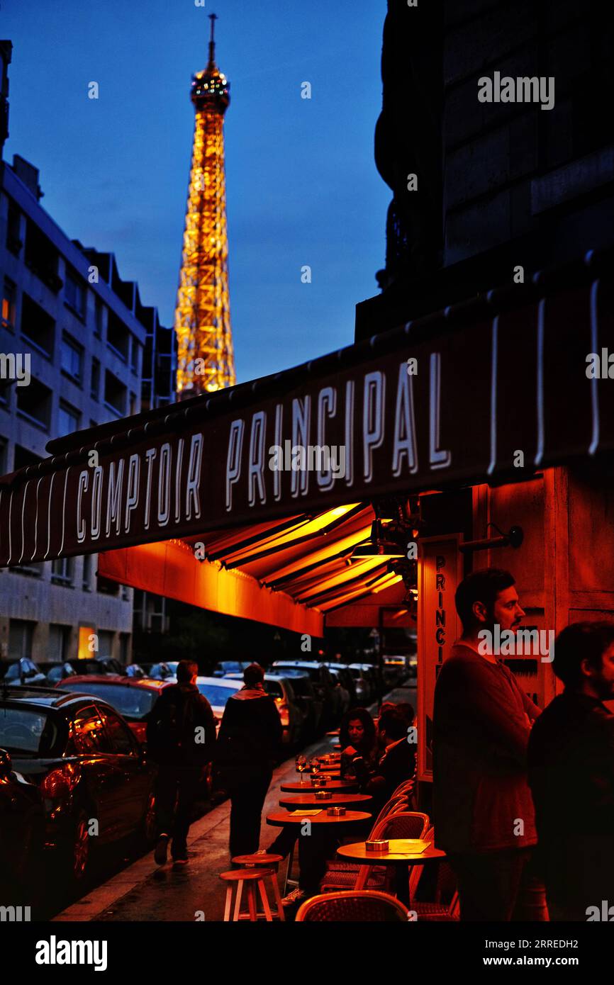 La Tour Eiffel illuminait au crépuscule sur un ciel bleu nocturne, l'auvent du Comptoir principal sur Grenelle brillant rouge, fin d'été, soir à Paris Banque D'Images