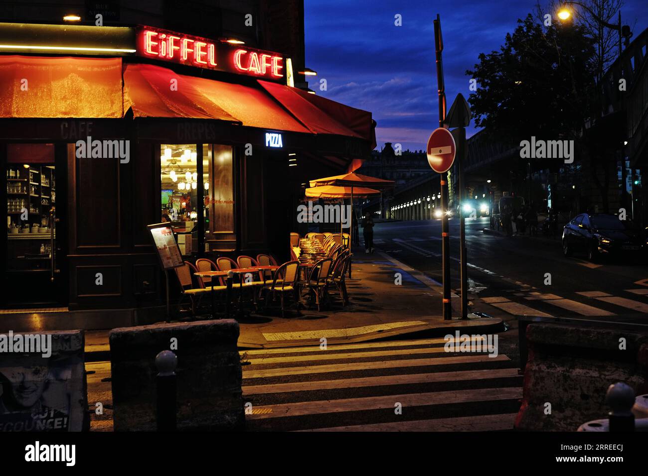 Café Eiffel en fin de soirée d'été, enseigne au néon rouge brillant sur le ciel bleu nocturne, chaises de café, lampadaires sur Grenelle et Pont de Bir-Hakeim Banque D'Images