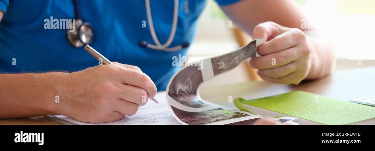 Un médecin de sexe masculin lit les antécédents médicaux du patient et prend des notes tout en travaillant au bureau. Banque D'Images