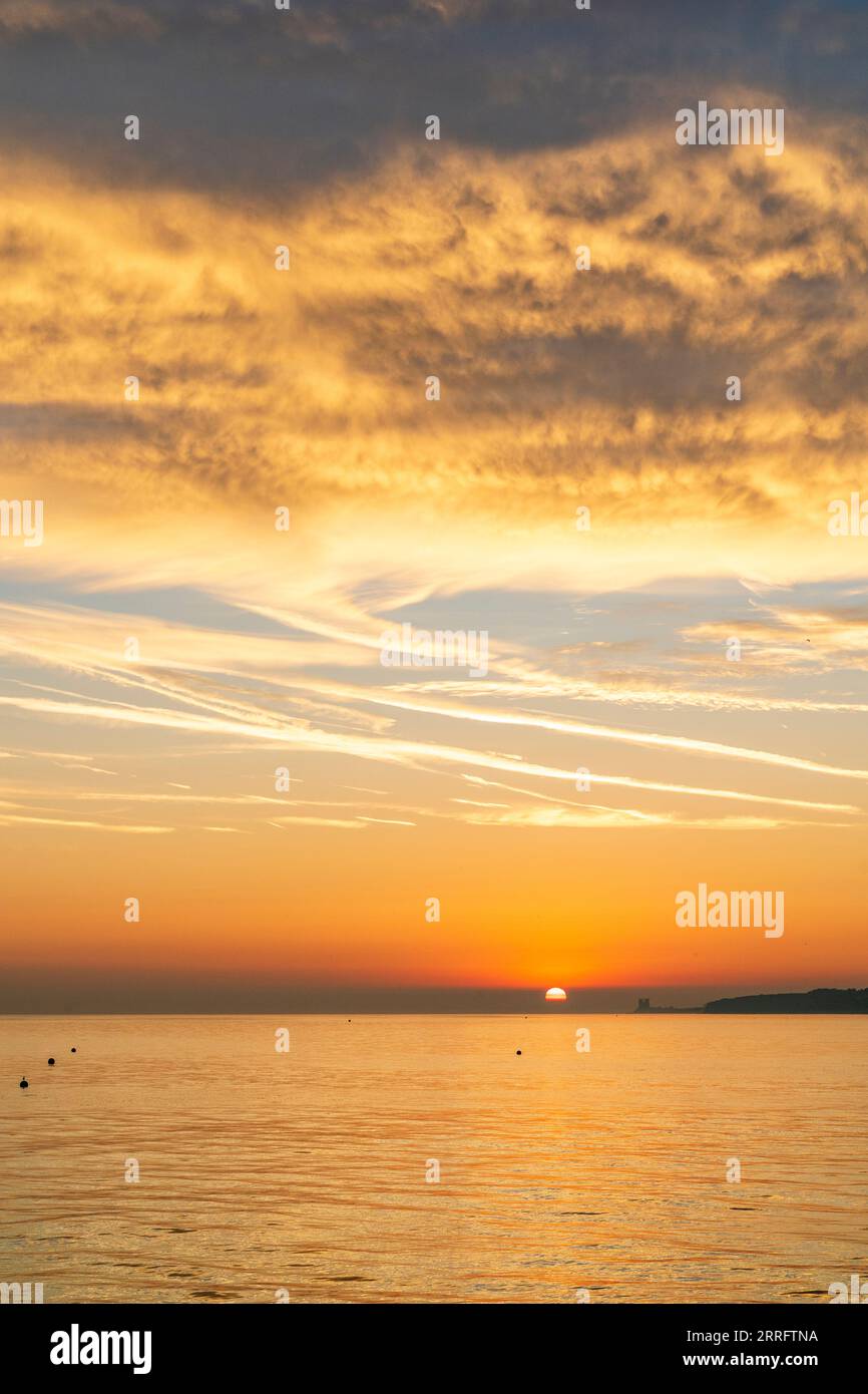 Lever de soleil sur la mer à la station balnéaire de Herne Bay, dans le nord du Kent. Nuages gris et jaunes spectaculaires sous l'éclairage du soleil levant à l'horizon. Bande de ciel orange avec la mer reflétant la couleur. Banque D'Images