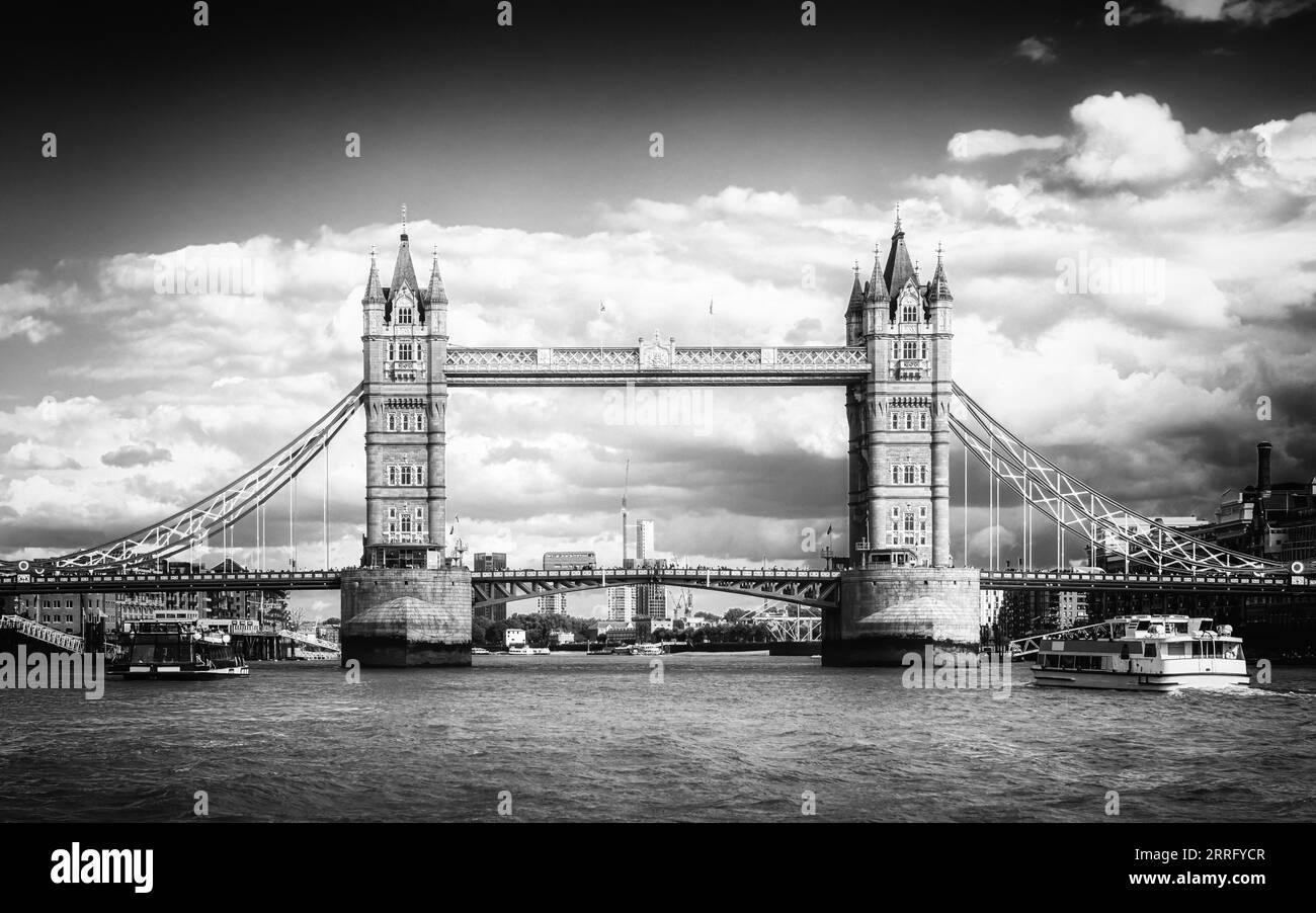 L'image en noir et blanc d'un bus londonien rouge emblématique passe au-dessus de Tower Bridge tandis que les bateaux de plaisance passent le long de la Tamise à Londres, en Angleterre Banque D'Images