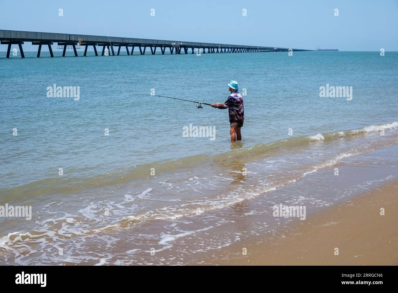 Un homme pêchant sur la plage de Lucinda avec Lucinda Jetty en arrière-plan, Queensland, Australie Banque D'Images