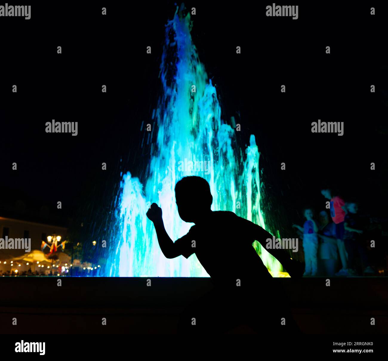 Place du marché de Krosno, vue sur la fontaine papale, la vieille ville de Krosno la nuit. Silhouette d'un garçon sur fond d'une fontaine colorée Banque D'Images