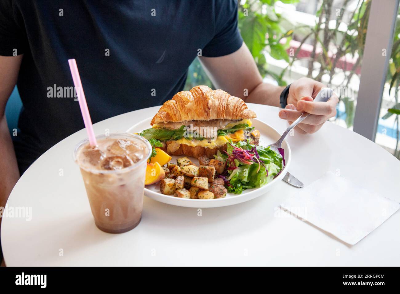 Mâle ayant délicieux petit déjeuner avec croissant sandwich et latte glacé. Banque D'Images