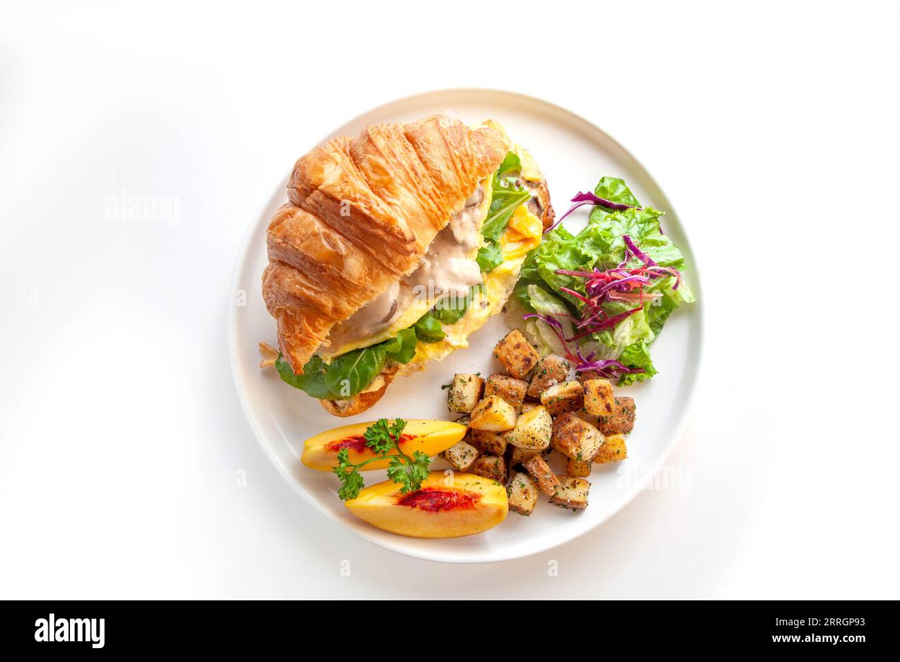 Brioche croissant oeuf brouillé Benedict avec champignons et crème avec pommes de terre sautées et fruits de pêche. Banque D'Images