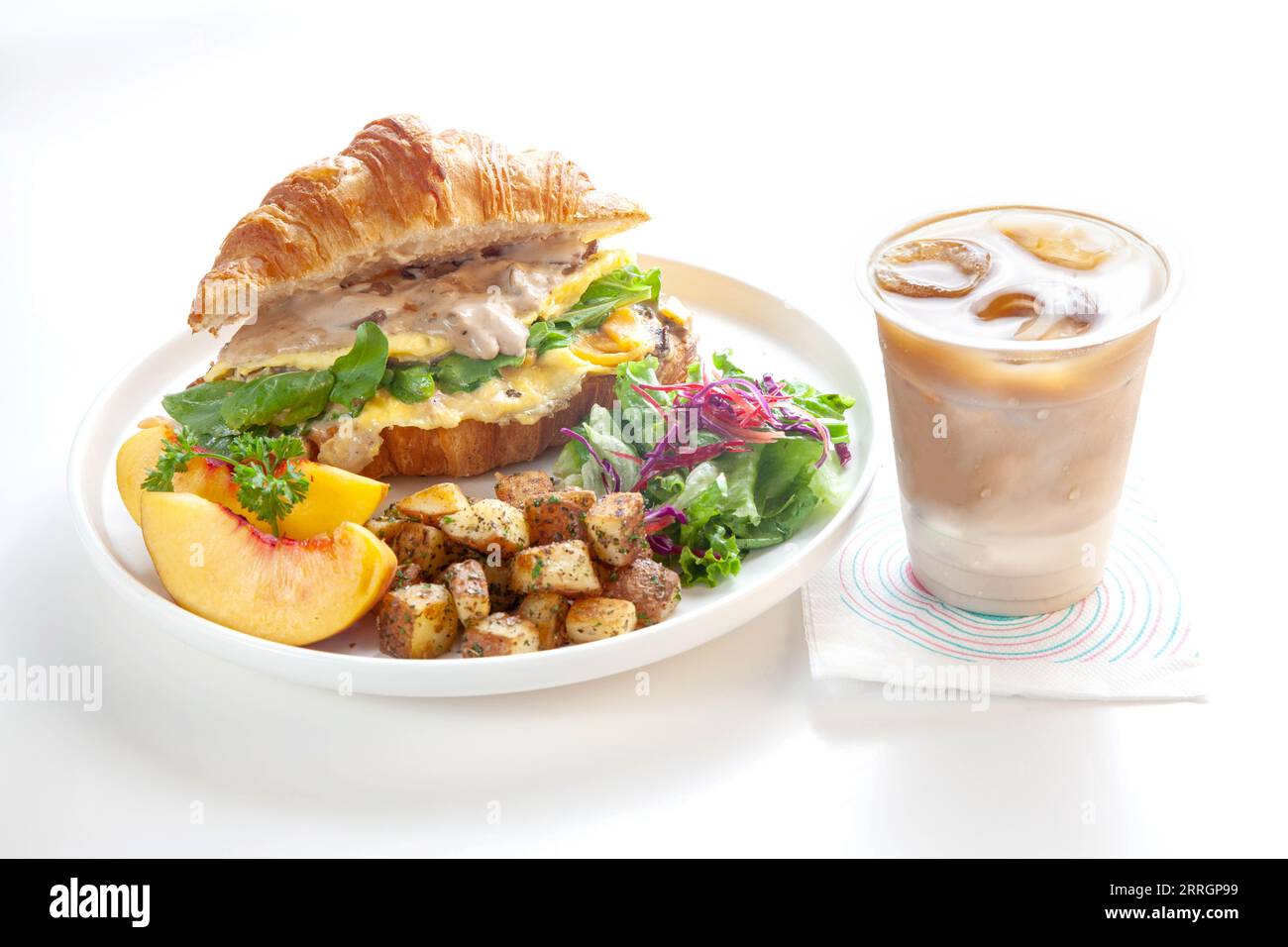 Brioche croissant oeuf brouillé Benedict avec champignons et crème avec pommes de terre sautées et fruits de pêche avec latte glacé. Banque D'Images