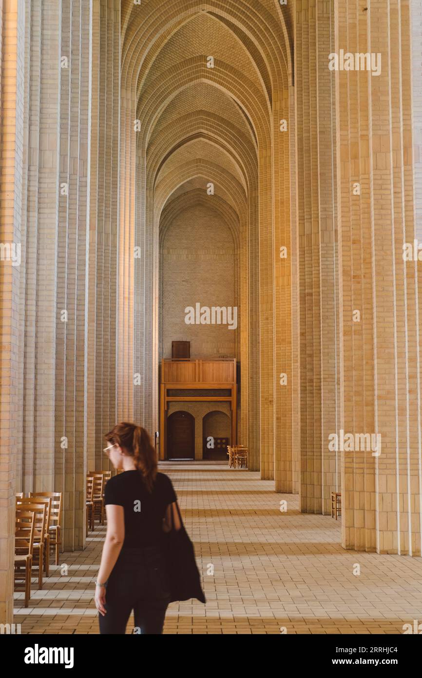 Intérieur de l'église de Grundtvig avec une figure de femme en noir marchant autour et de grandes colonnes verticales en pierre et sol carrelé Banque D'Images