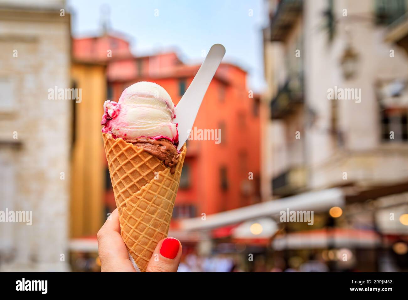 Main de femme tenant du chocolat artisanal et du gelato amarena dans un cône, vue sur les maisons colorées traditionnelles dans la vieille ville de Nice, sud de la France Banque D'Images