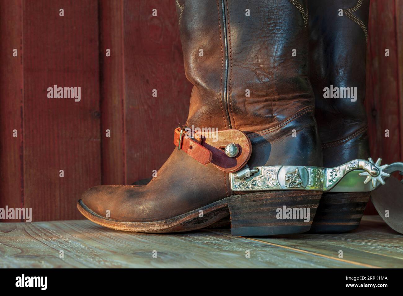 Vieilles bottes de cow-boy en cuir marron avec éperons sur une surface en bois à la lumière du soleil Banque D'Images