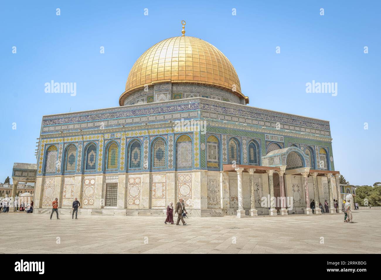 Plusieurs individus se promènent sur le trottoir devant un édifice aux dômes dorés étincelants Banque D'Images