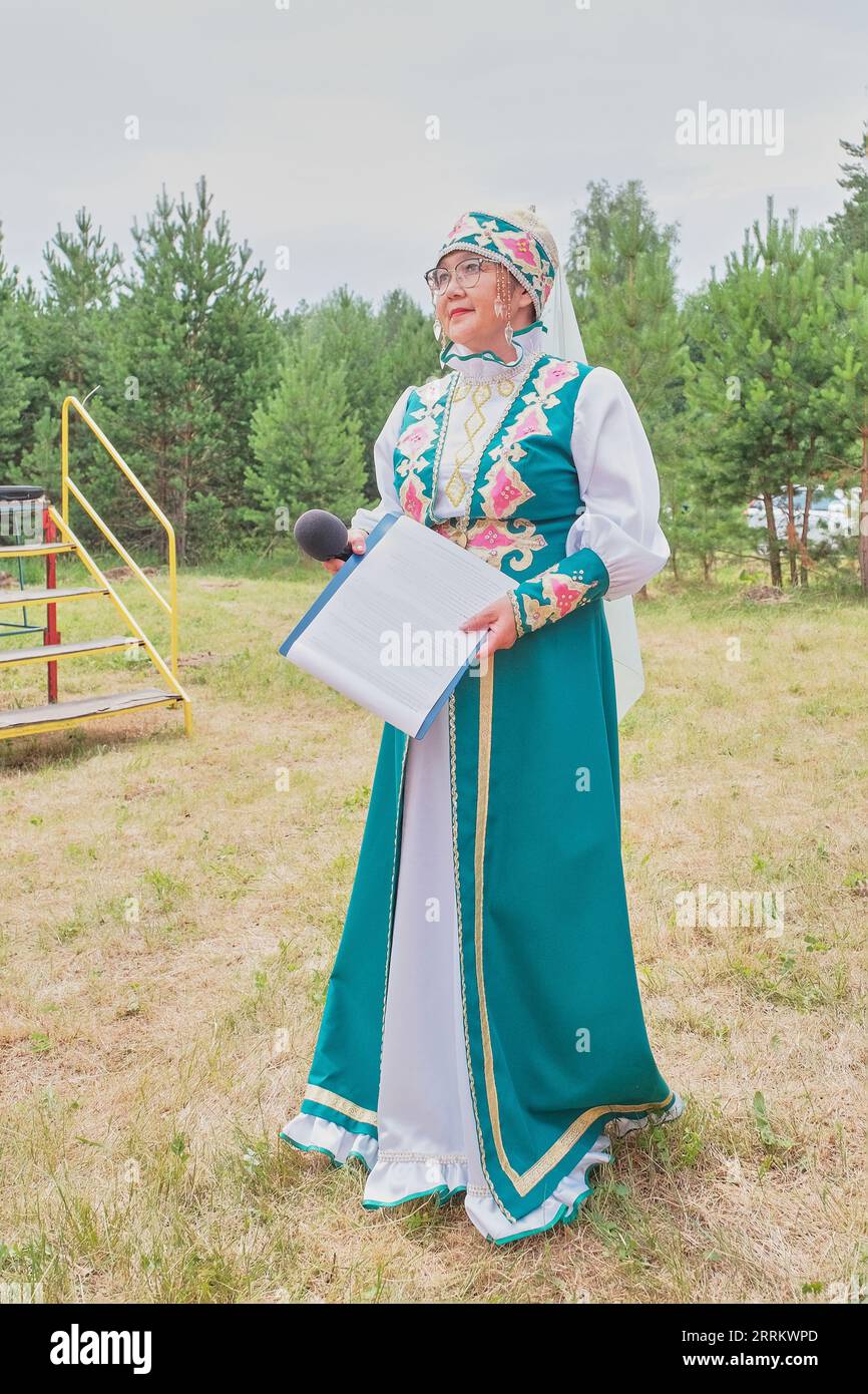 Portrait en pied de l'hôte du concert au festival du village. Femme asiatique mature dans des vêtements stylisés de Tatars ethniques avec microphone près de la scène. Jour du s Banque D'Images