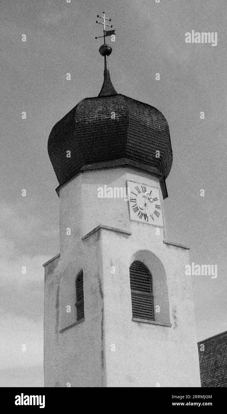 Tyrol, Autriche. c.1960 – l'horloge/le clocher de St. Église Antoine de Padoue située sur Dorfstraße à St Anton am Arlberg. La tour a un toit en dôme en « oignon » carrelé surmonté de la Croix de Lorraine avec girouette intégrée. La tour a une horloge avec des fenêtres à persiennes ci-dessous. Banque D'Images