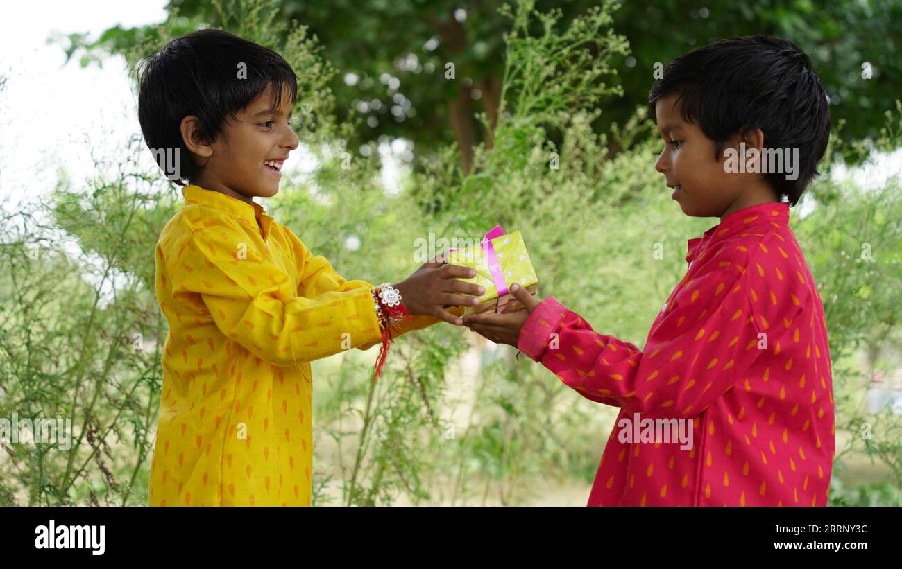 Frère et sœur hindous en vêtements ethniques tenant des bonbons indiens et boîte cadeau à l'occasion du festival Raksha Bandhan Banque D'Images