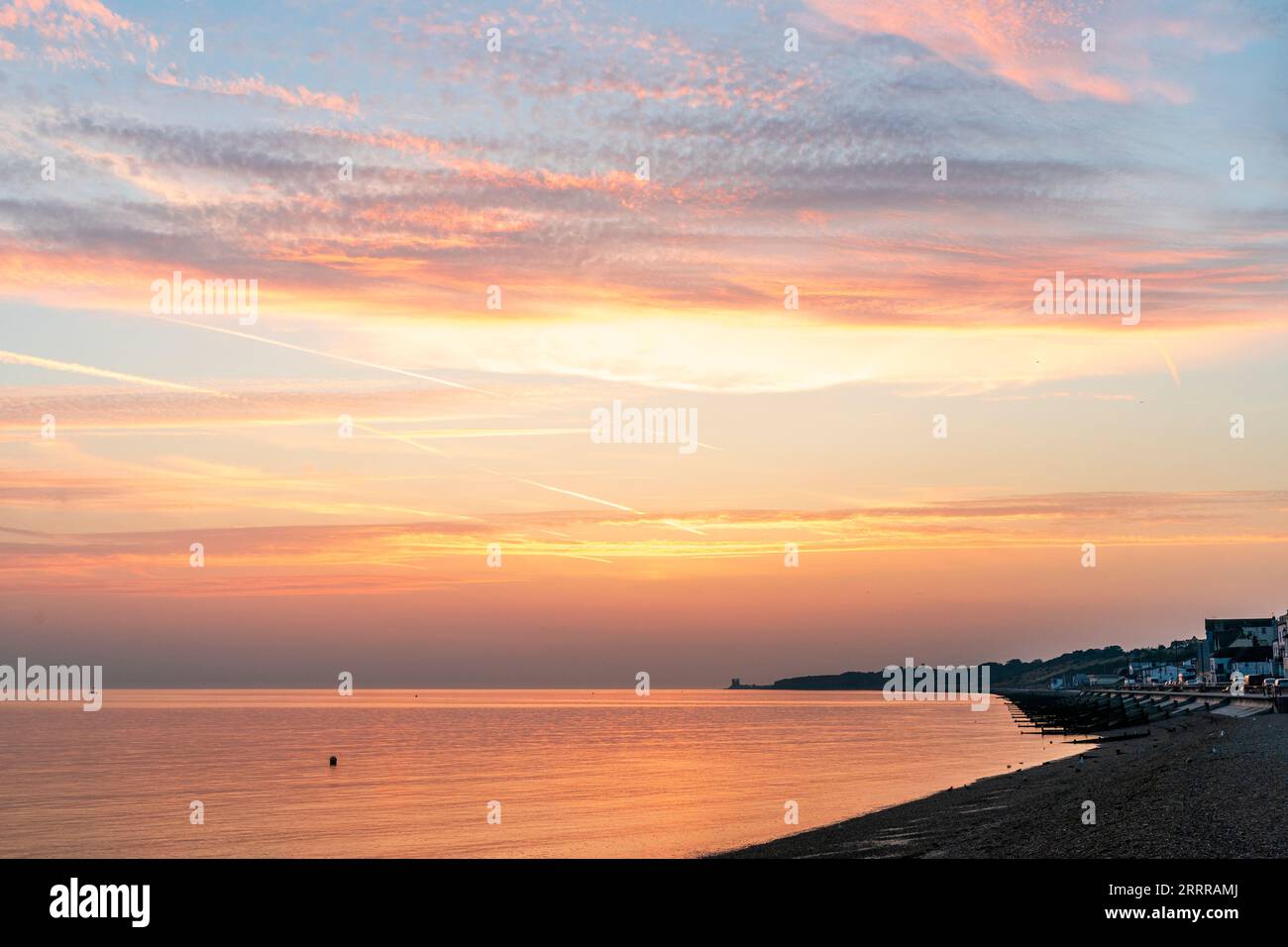 Le ciel de l'aube sur la plage du front de mer et la mer à Herne Bay sur la côte nord du Kent. Quelques couches de nuage jaune et orange contre un ciel bleu. Mer orange reflétant la lumière. Banque D'Images
