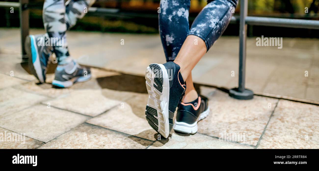 Vue de taille vers le bas de coureuse femme méconnaissable avec une jambe croisée reposant à côté de ses amies féminines après l'entraînement de nuit sur la ville Banque D'Images