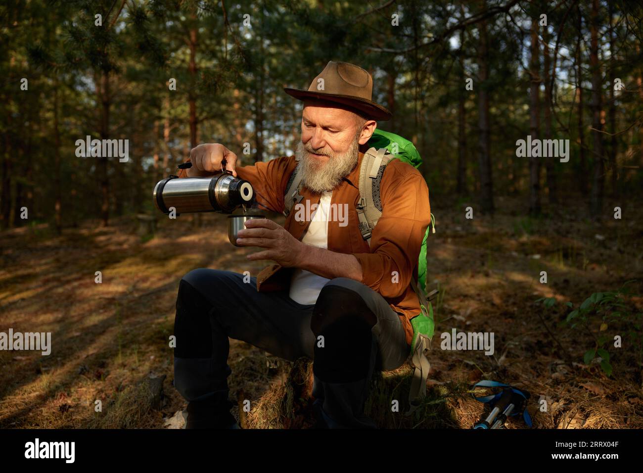 Homme senior randonneur buvant du thé chaud de la tasse thermos dans la forêt Banque D'Images