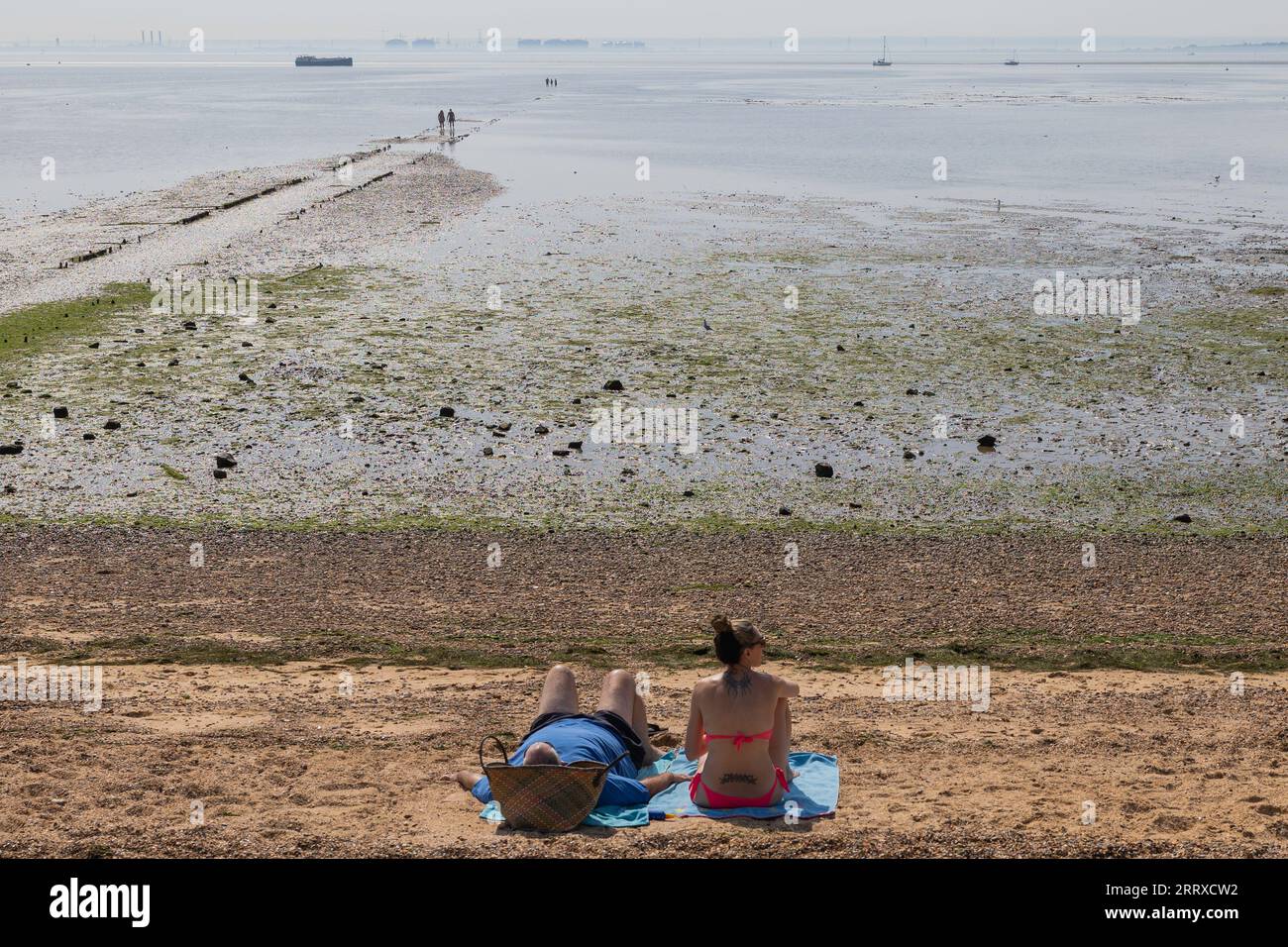 Southend on Sea, Royaume-Uni. 9 septembre 2023. Deux personnes se détendent sur des serviettes à Southend Beach pendant la marée basse, avec des taches d'algues visibles sur le sable exposé. Un moment côtier tranquille avec des marcheurs lointains et des navires faibles à l'horizon. Le jour a été provisoirement nommé le jour le plus chaud de l'année jusqu'à présent, avec 32.7C enregistrés, et le sixième jour consécutif de températures dépassant 30c. Penelope Barritt/Alamy Live News Banque D'Images