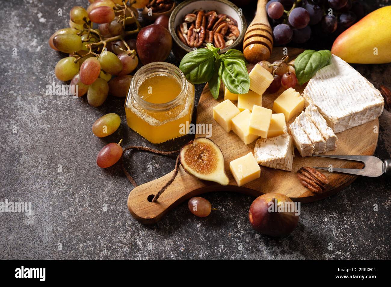 Fromage brie, figues fraîches, raisins, cubes de fromage, poires, noix de pécan et miel sur planche à découper sur fond de pierre sombre. Assiette à fromage, nature morte des mers Banque D'Images