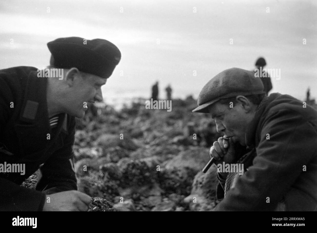 Ein Muschelernter am Strand von le Havre zeigt dem Fotografen Erich Andres in der Uniform der Kriegsmarine, wie man Muscheln erntet, öffnet und isst, 1940. Une récolteuse de moules sur la plage du Havre montre au photographe Erich Andres dans son uniforme de Kriegsmarine comment récolter, ouvrir et manger des moules, 1940. Banque D'Images