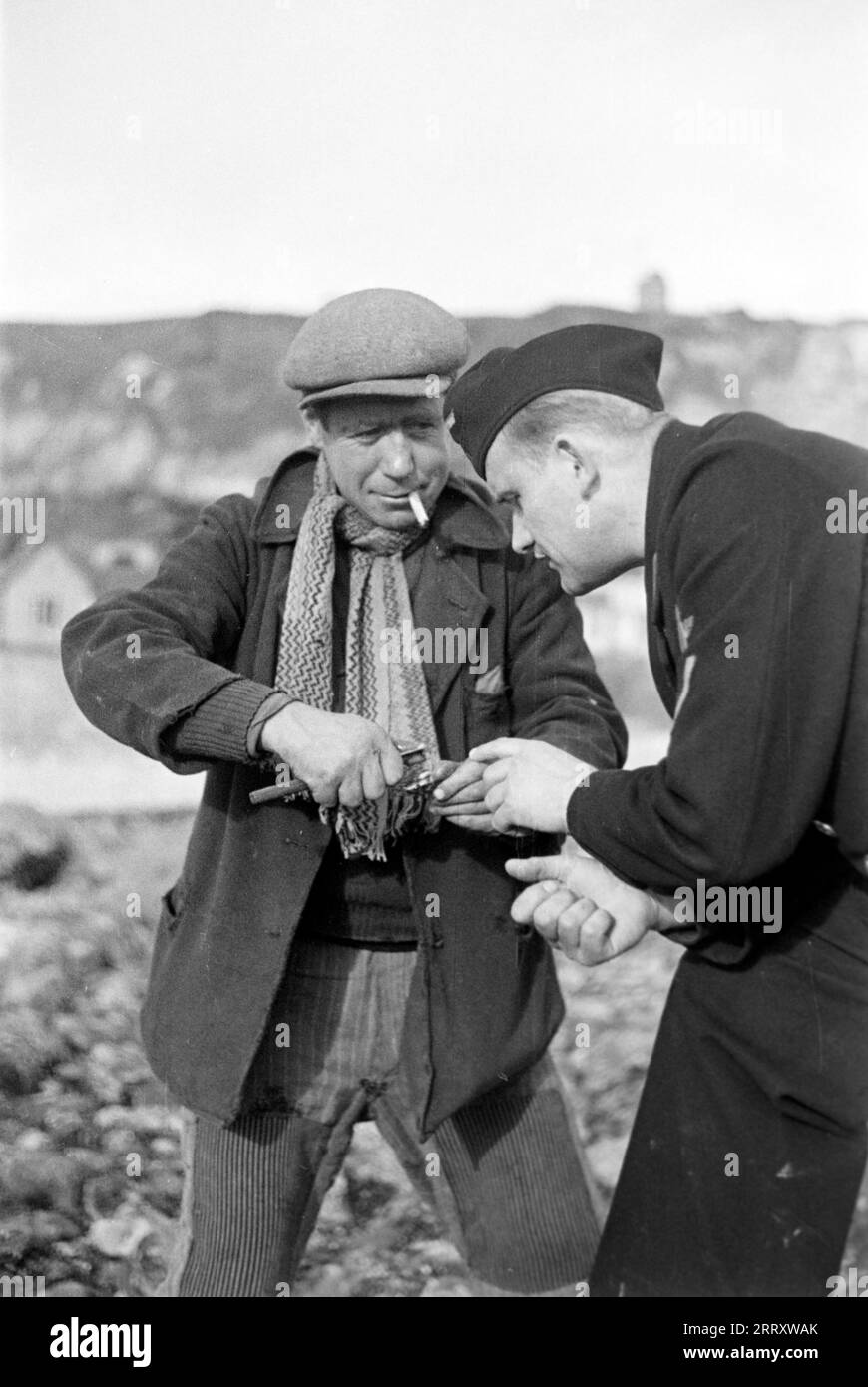 Ein Muschelernter am Strand von le Havre zeigt dem Fotografen Erich Andres in der Uniform der Kriegsmarine, wie man Muscheln erntet, öffnet und isst, 1940. Une récolteuse de moules sur la plage du Havre montre au photographe Erich Andres dans son uniforme de Kriegsmarine comment récolter, ouvrir et manger des moules, 1940. Banque D'Images