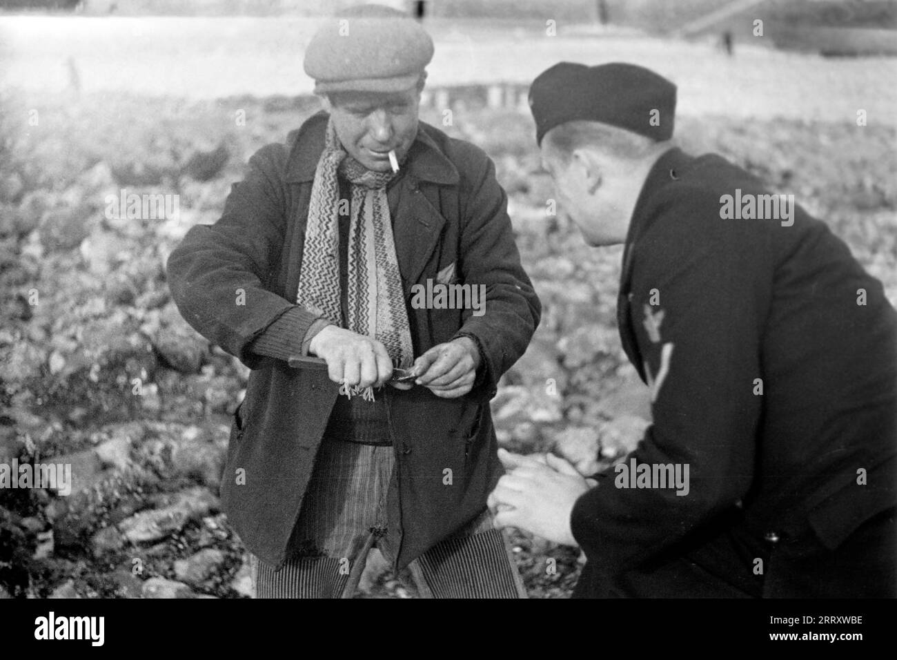 Ein Muschelernter am Strand von le Havre zeigt dem Fotografen Erich Andres in der Uniform der Kriegsmarine, wie man Muscheln erntet, öffnet und isst, 1940. Une récolteuse de moules sur la plage du Havre montre au photographe Erich Andres dans son uniforme de Kriegsmarine comment récolter, ouvrir et manger des moules, 1940. Banque D'Images