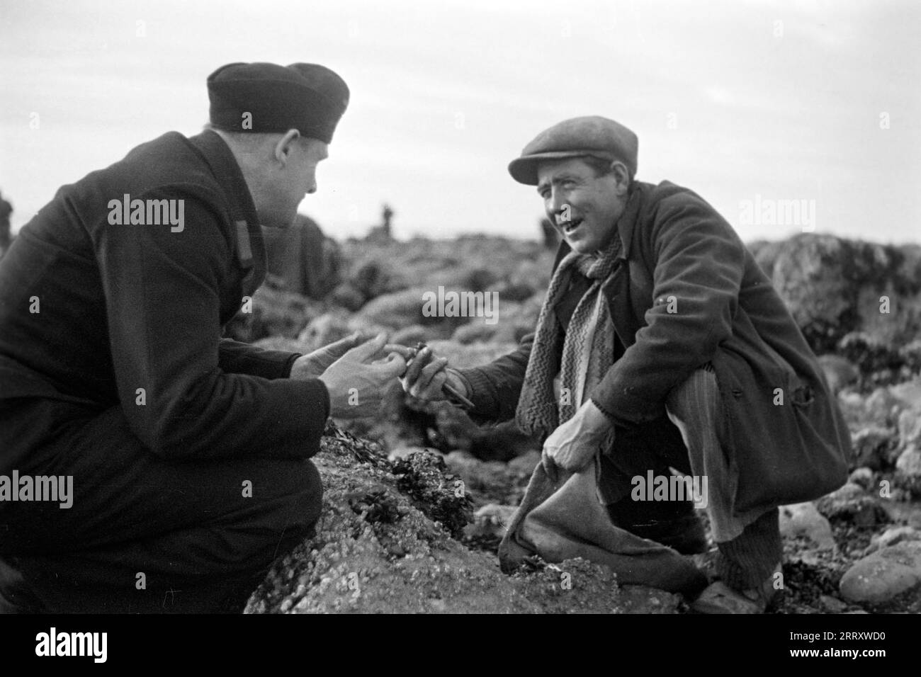Ein Muschelernter am Strand von le Havre zeigt dem Fotografen Erich Andres in der Uniform der Kriegsmarine, wie man Muscheln erntet, öffnet und isst, 1940. Une récolteuse de moules sur la plage du Havre montre au photographe Erich Andres dans son uniforme de Kriegsmarine comment récolter, ouvrir et manger des moules, 1940. Banque D'Images