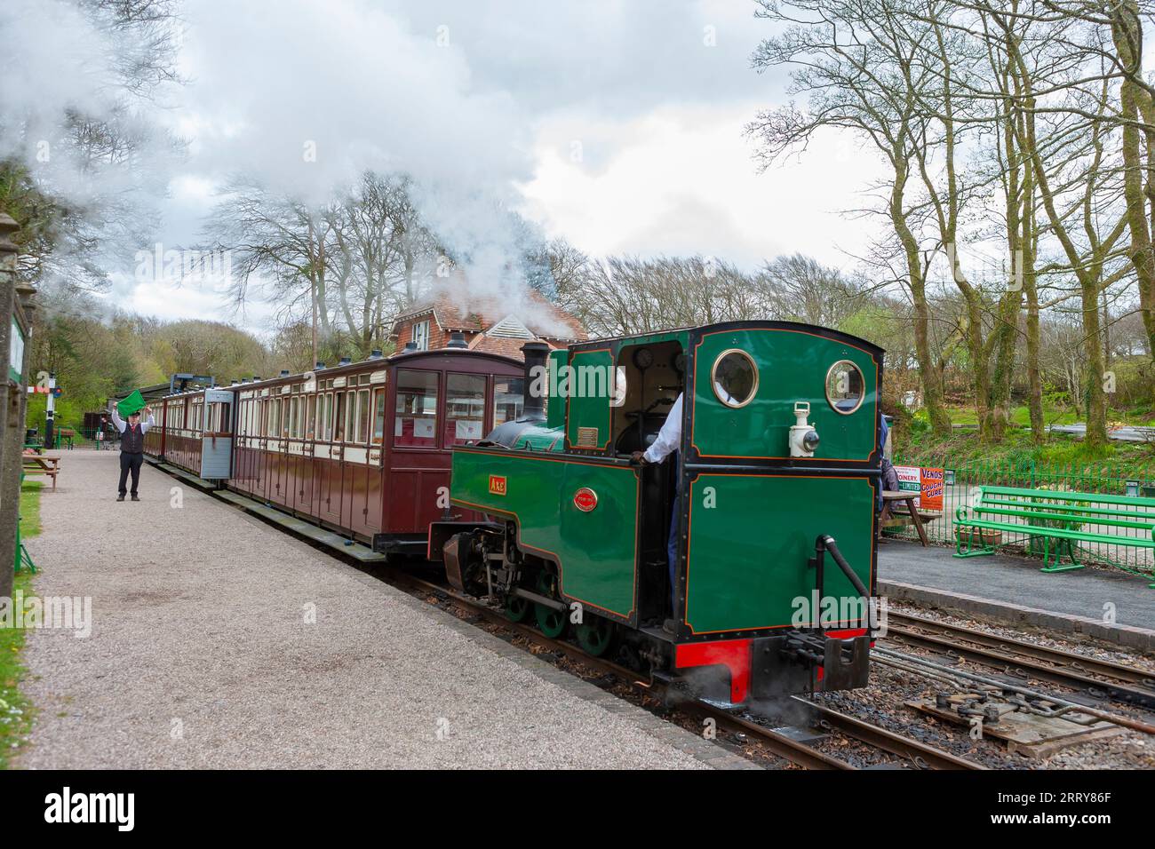 La garde agite le drapeau vert alors que le train à vapeur à voie étroite tiré par « axe » quitte la gare de Woody Bay sur la Lynton and Barnstaple Railway, Devon, Royaume-Uni Banque D'Images