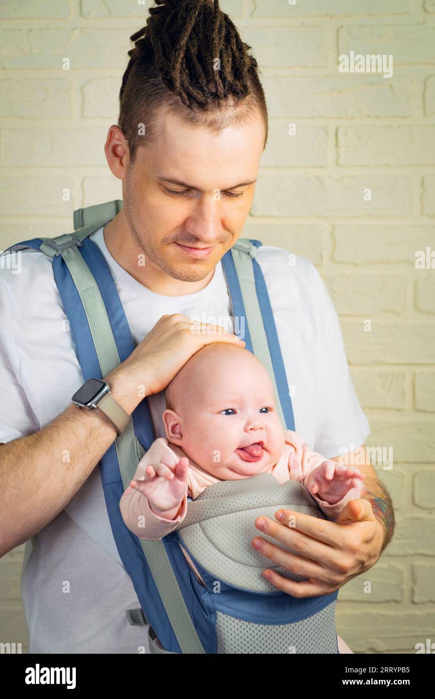 jeune père avec son bébé nouveau-né dans une écharpe, sur un fond de mur de briques Banque D'Images