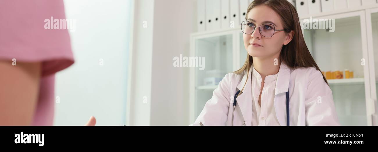 Un jeune médecin écoute sa patiente tout en étant assis à la table de la clinique médicale. Banque D'Images