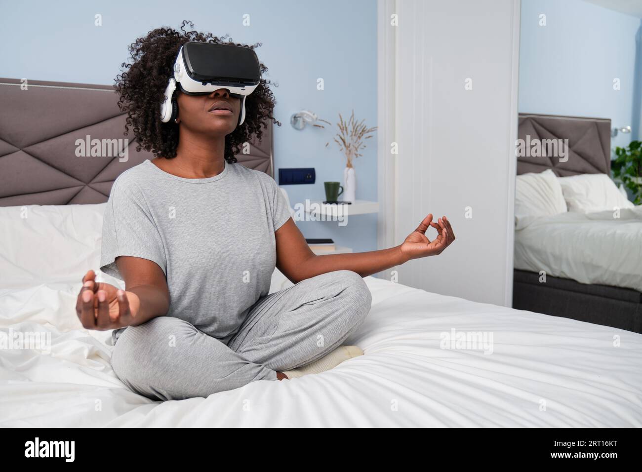 Jeune femme africaine méditant avec des lunettes VR assis sur le lit. Banque D'Images