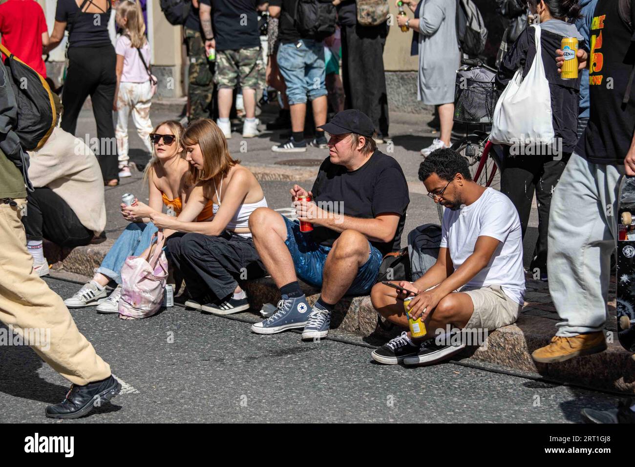 Des jeunes assis sur un trottoir avec des boissons à Kallio Block Party 2023 par une journée ensoleillée d'été à Helsinki, Finlande Banque D'Images