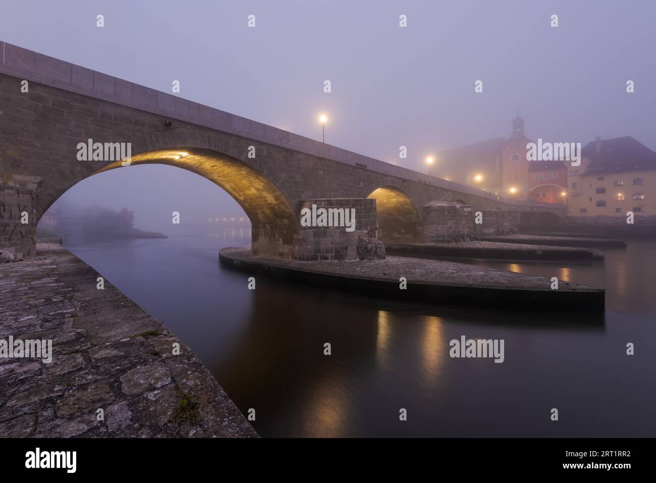 Le pont de pierre dans la ville bavaroise de Ratisbonne avant l'aube couvert d'un épais brouillard d'automne Banque D'Images