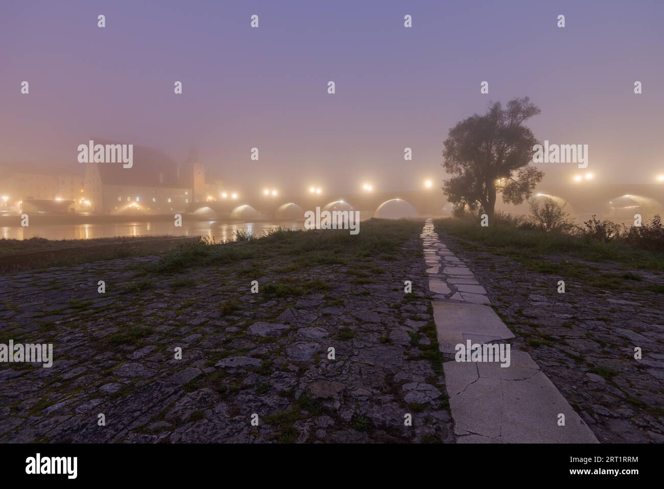 Le pont de pierre dans la ville bavaroise de Ratisbonne avant l'aube couvert d'un épais brouillard d'automne Banque D'Images