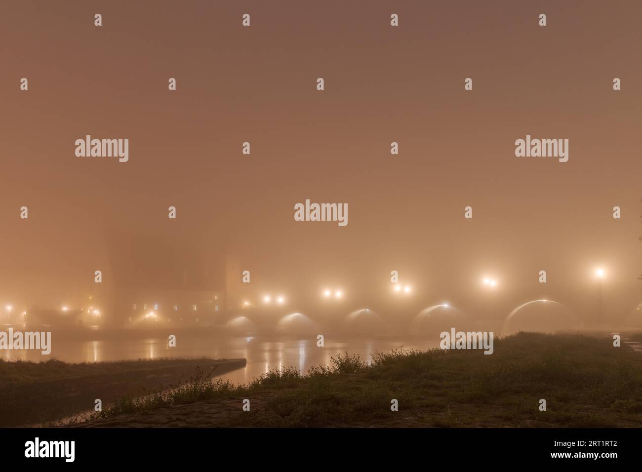 Le pont de pierre dans la ville bavaroise de Ratisbonne avant l'aube couvert d'un épais brouillard d'automne Banque D'Images