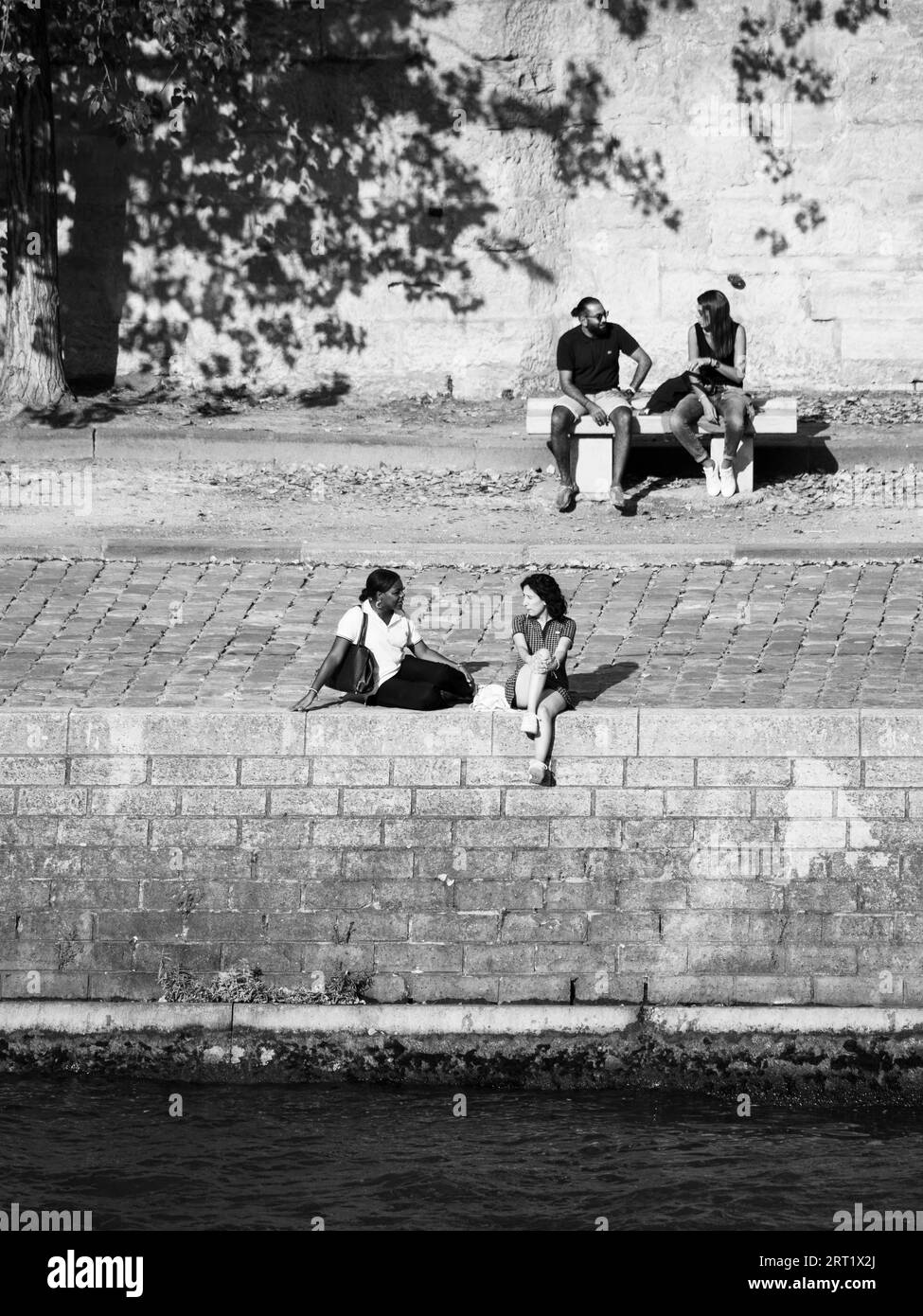 B&W personnes se détendant sur la rive de la Seine, Île Saint-Louis, île dans la Seine, Paris, France, Europe, UE. Banque D'Images