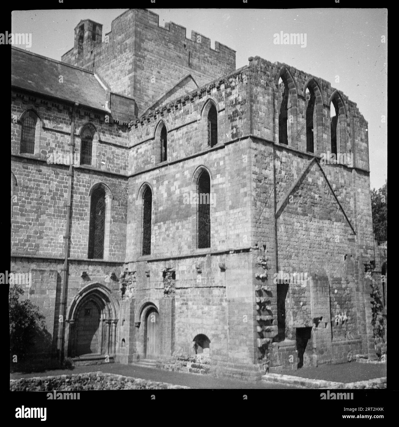 Lanercost Prieuré, Lanercost, Burtholme, Carlisle, Cumbria, 1940-1962. Vue extérieure des ruines du Prieuré de Lanercost, très probablement du côté sud. Le côté droit de l'image montre une section de trois étages de l'ancien prieuré, peut-être le transept sud, qui a une petite entrée en arc rond sur le côté ouest dans le coin, et une forme de triangle au-dessus du deuxième étage sur le côté sud. À droite se trouve la nef du prieuré, qui est encore utilisée comme église paroissiale, l'église Sainte-Marie. Toute la hauteur de l'ancienne nef est visible, avec le toit en tuiles intact. En arrière-plan se trouve le rema Banque D'Images