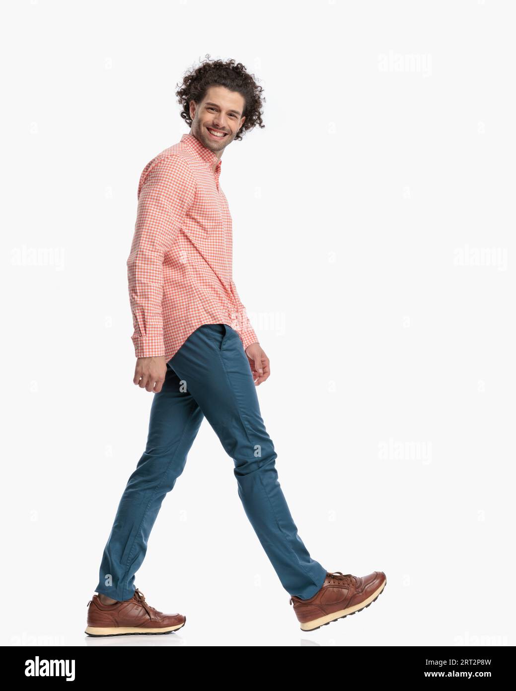 image complète du corps de gars occasionnel heureux avec les cheveux bouclés souriant et marchant devant le fond blanc dans le studio Banque D'Images