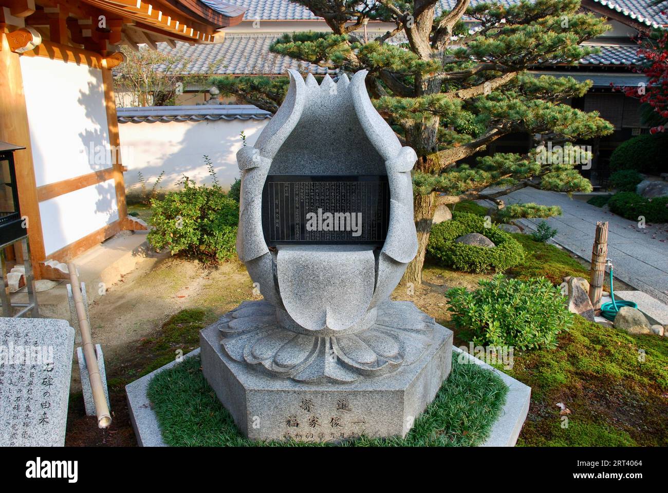 Une sculpture en pierre de style asiatique tranquille représentant une fleur de lotus reposant au milieu d'un feuillage luxuriant dans un parc pittoresque Banque D'Images