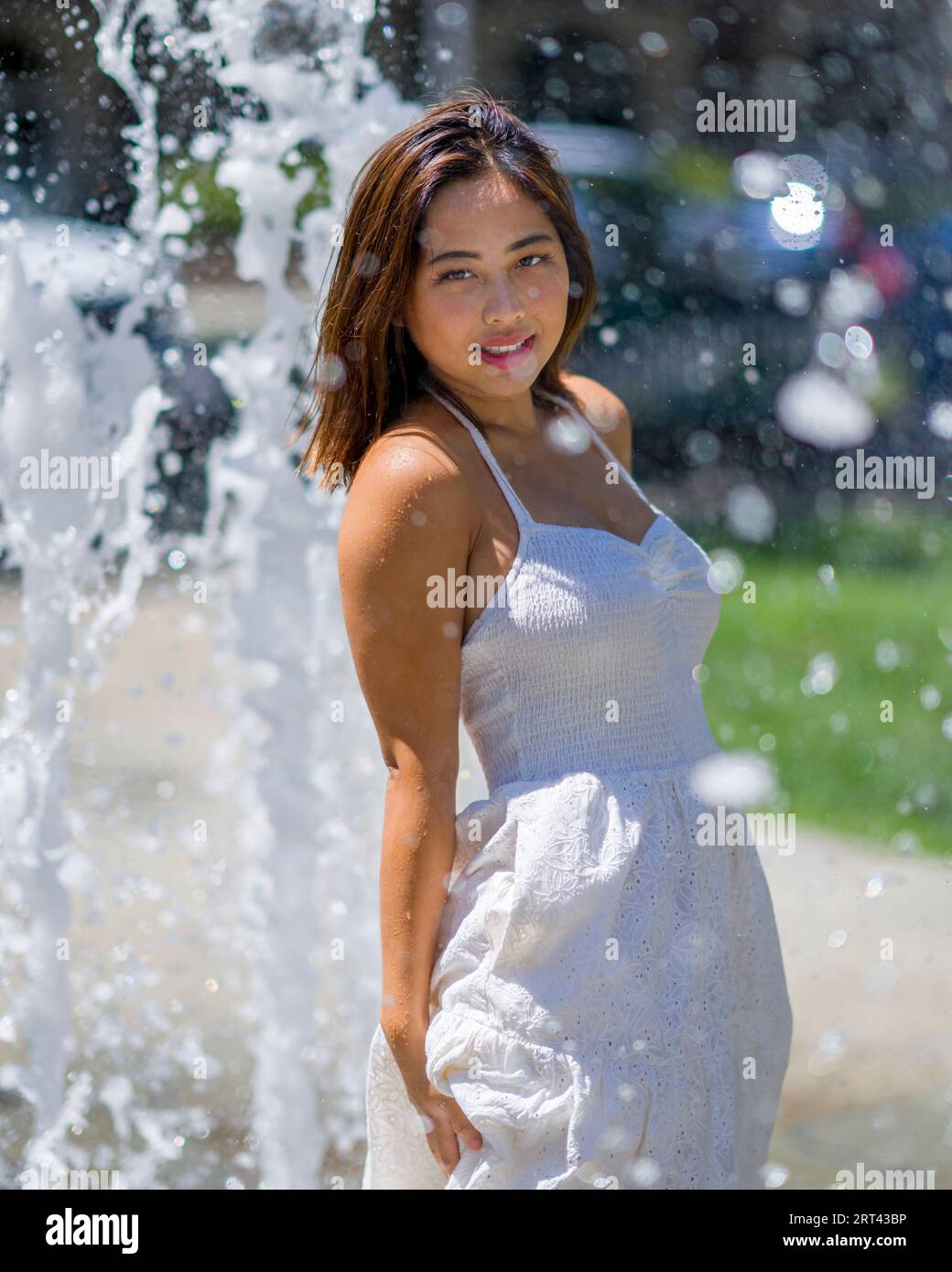 Belle jeune femme asiatique heureuse jouant dans la fontaine extérieure sur une journée chaude ensoleillée | White Sundress Banque D'Images