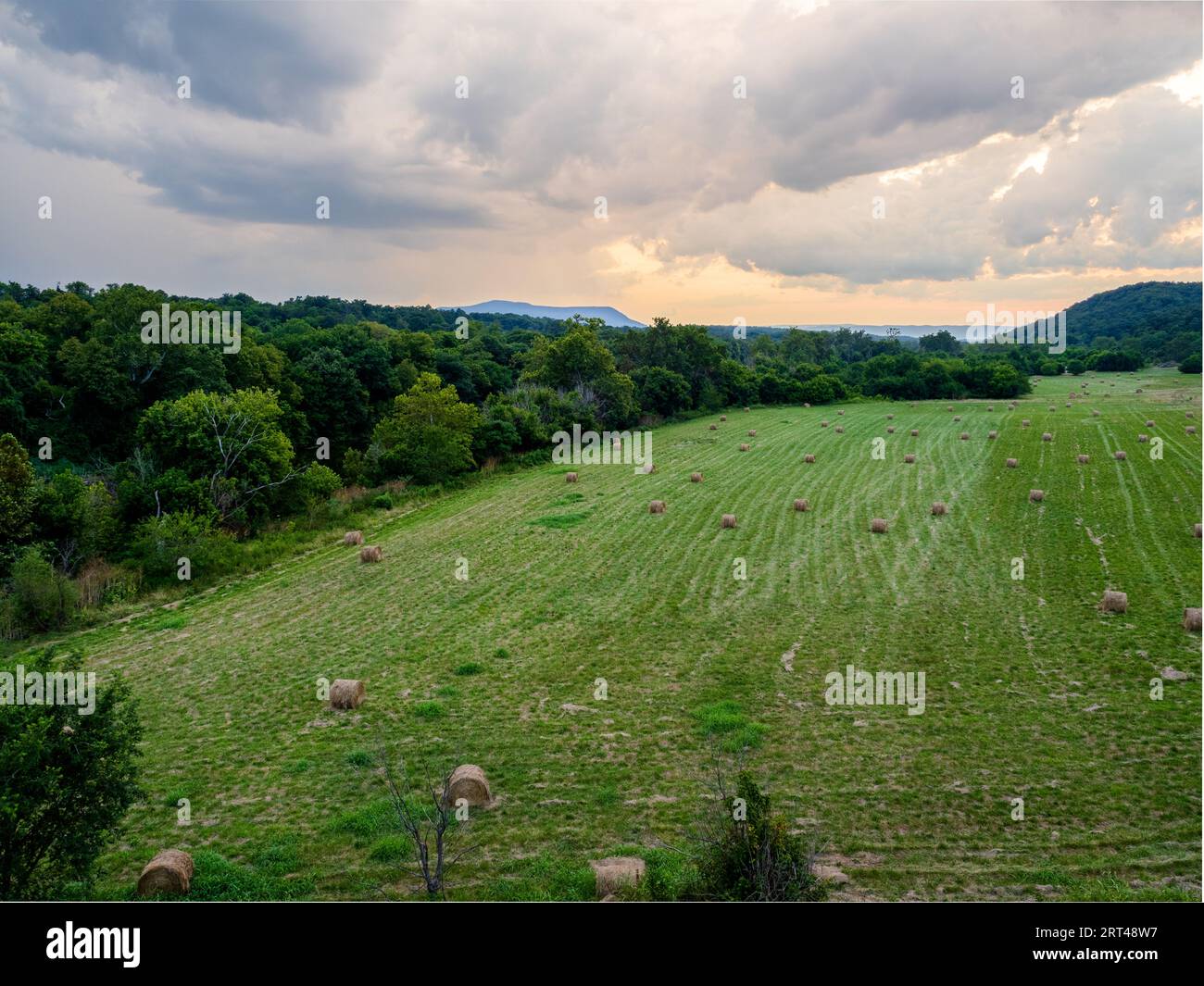 Un champ ouvert avec des balles de foin surplombant la vallée de Shenandoah, baigné dans les teintes chaudes des nuages de coucher de soleil, près de Front Royal, Virginie, États-Unis. Banque D'Images