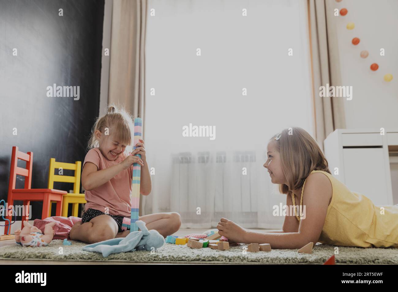 Enfants jouant avec des jouets colorés. Enfants assis sur la moquette dans la chambre à coucher ou la maternelle à la maison, la crèche. Jeu écologique éducatif pour enfant. Intérieur de la chambre des enfants. Mess sur le sol. Espace de copie Banque D'Images