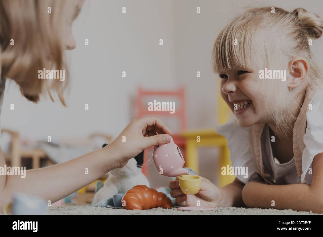 Gros plan d'enfants de sexe féminin jouant avec un ensemble de thé de jeu de jouet coloré. Enfants assis sur tapis à la maison ou à la maternelle, garderie. Jeux écologiques éducatifs. Développement de la motricité, imagination Banque D'Images