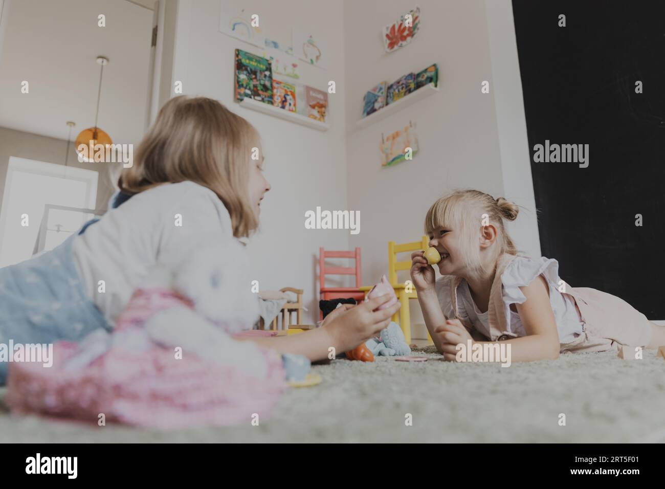 Les enfants jouant avec un ensemble de thé de jeu en plastique coloré. Les enfants assis sur le tapis à l'intérieur à la chambre à coucher blanche ensoleillée à la maison ou à la maternelle, garderie. Jeu amusant et écologique éducatif pour enfant. Deux sœurs Banque D'Images