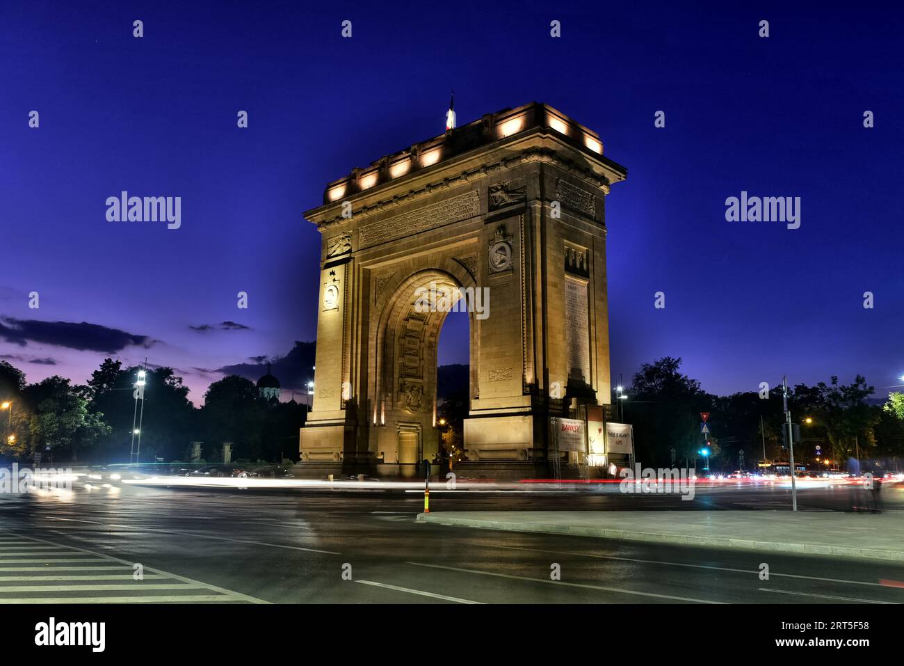 Arcul de TRIUMF sur Kiseleff Road, Bucarest, Roumanie. La traînée légère de la circulation de banlieue du soir a fait brûler un crépuscule d'admiste en cercle complet Banque D'Images