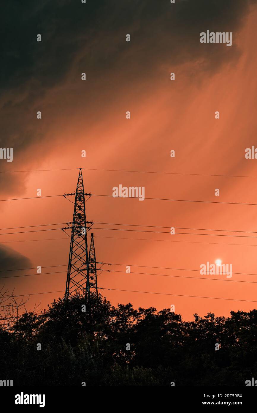 Nuages orageux sombres au ciel orange d'été, silhouettes de cimes d'arbres et pylône électrique juste avant la pluie, mise au point sélective Banque D'Images