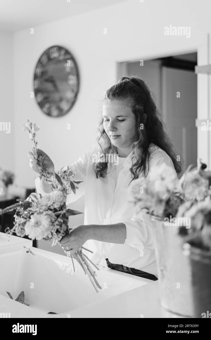 Une femme arrangeant un bouquet de fleurs au-dessus de l'évier dans sa cuisine Banque D'Images