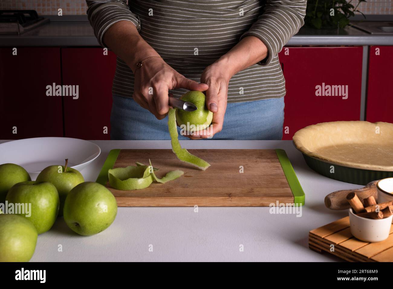 La femme épluche les pommes pour préparer la tarte aux pommes dans la cuisine. Les mains féminines authentiques épluchent une pomme avec un couteau. Cuisson de la tarte aux pommes, étape de recette Banque D'Images