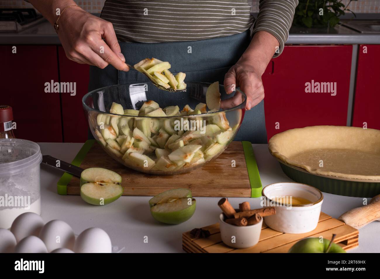 Femme mélangeant des pommes coupées dans un bol avec des épices, cannelle, anice, sucre, cuisson de tarte aux pommes dans la cuisine entourée d'autres ingrédients, Thanksgivi Banque D'Images